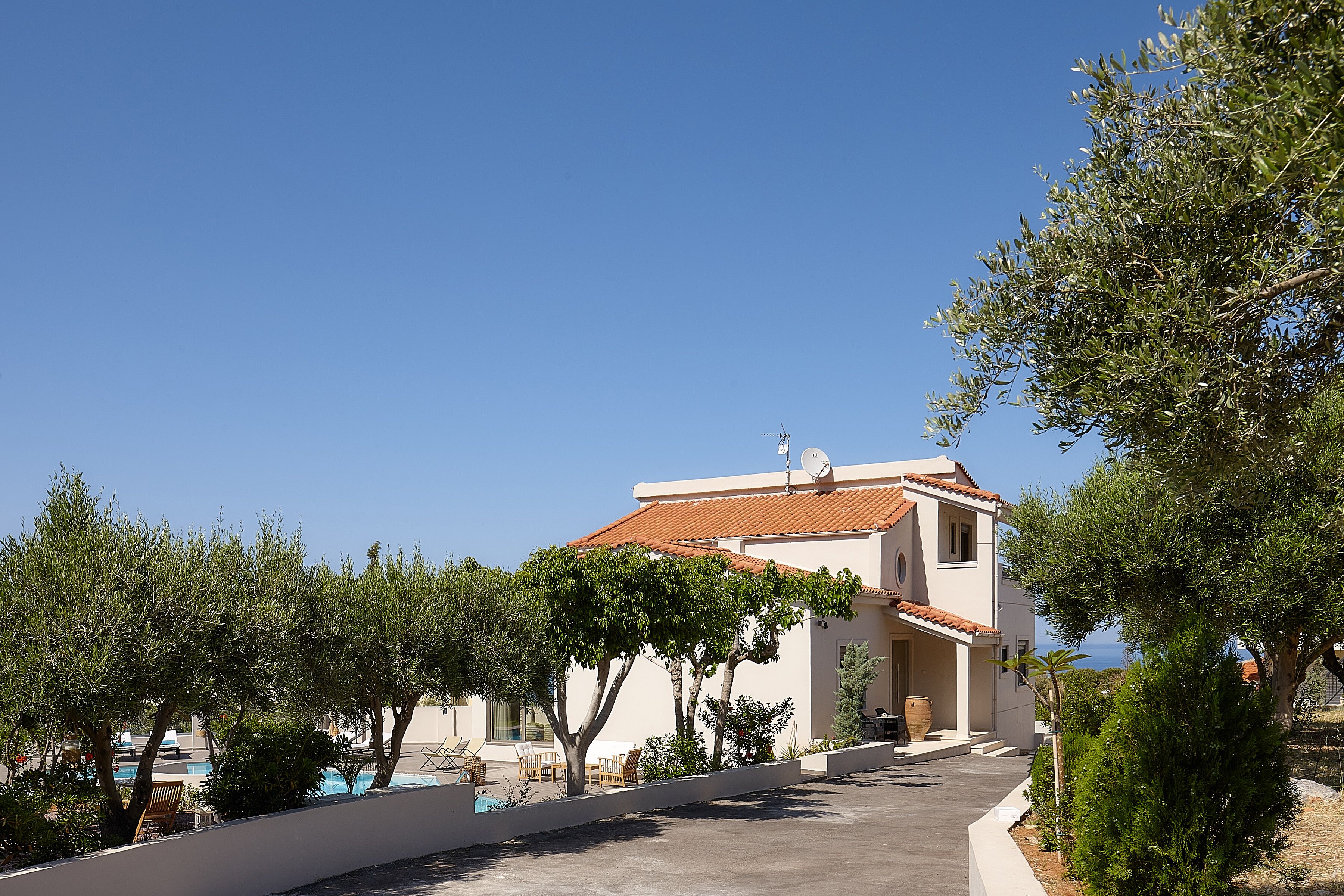 A two-story building with a tiled roof, a swimming pool, and a clear blue sky.