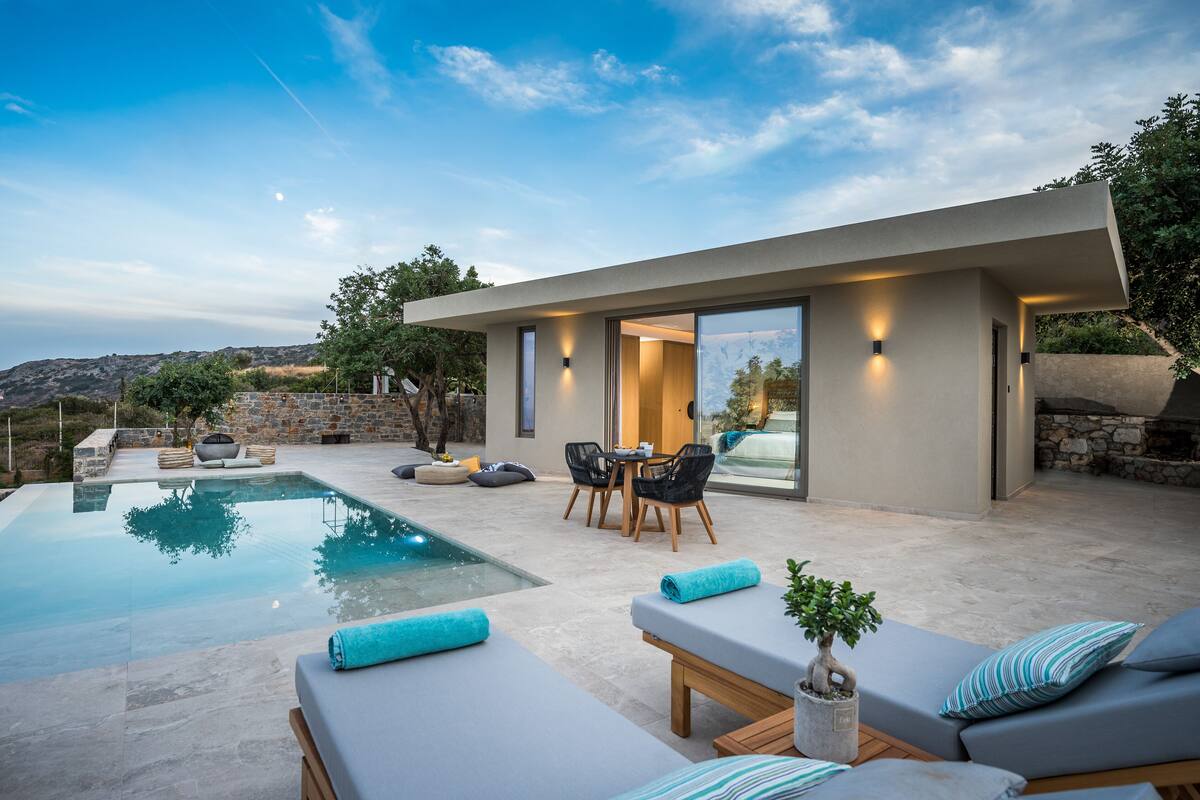 Un área de piscina moderna al aire libre, con solárium, mobiliario y un muro de piedra de fondo.