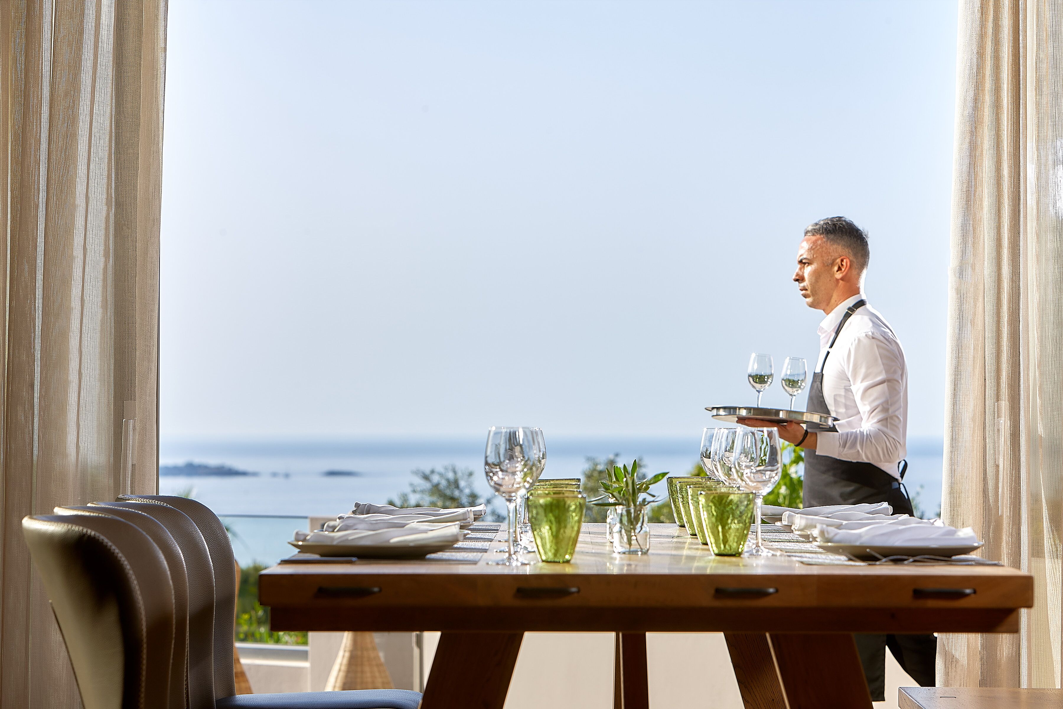 A dining table set for a meal with a view of the ocean.