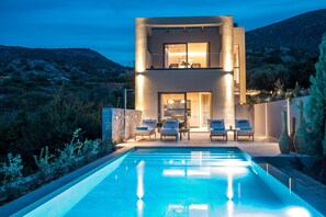 Una casa moderna de dos pisos con piscina, mobiliario exterior y vistas del paisaje circundante.