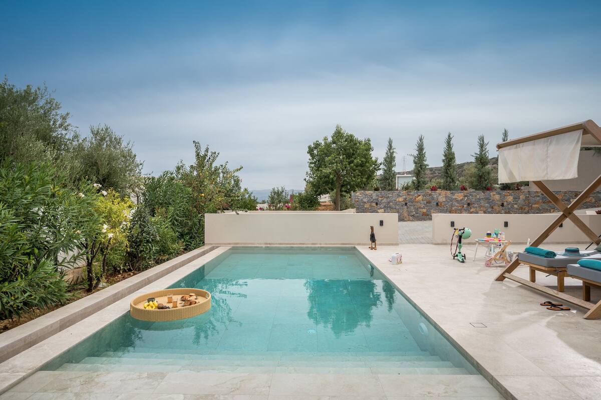 Una piscina con una cesta flotante, sillas de descanso y un muro de piedra al fondo.