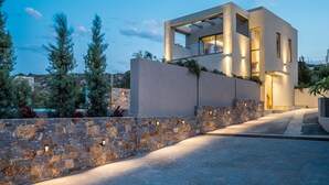 A modern house with a stone wall, a balcony, and a well-lit entrance. -  Grace Villas Collection (Hersonissos)