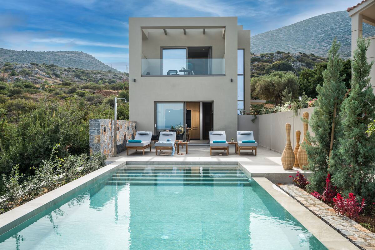 Un moderno edificio de dos pisos con piscina, zona de estar al aire libre y vistas del paisaje circundante.