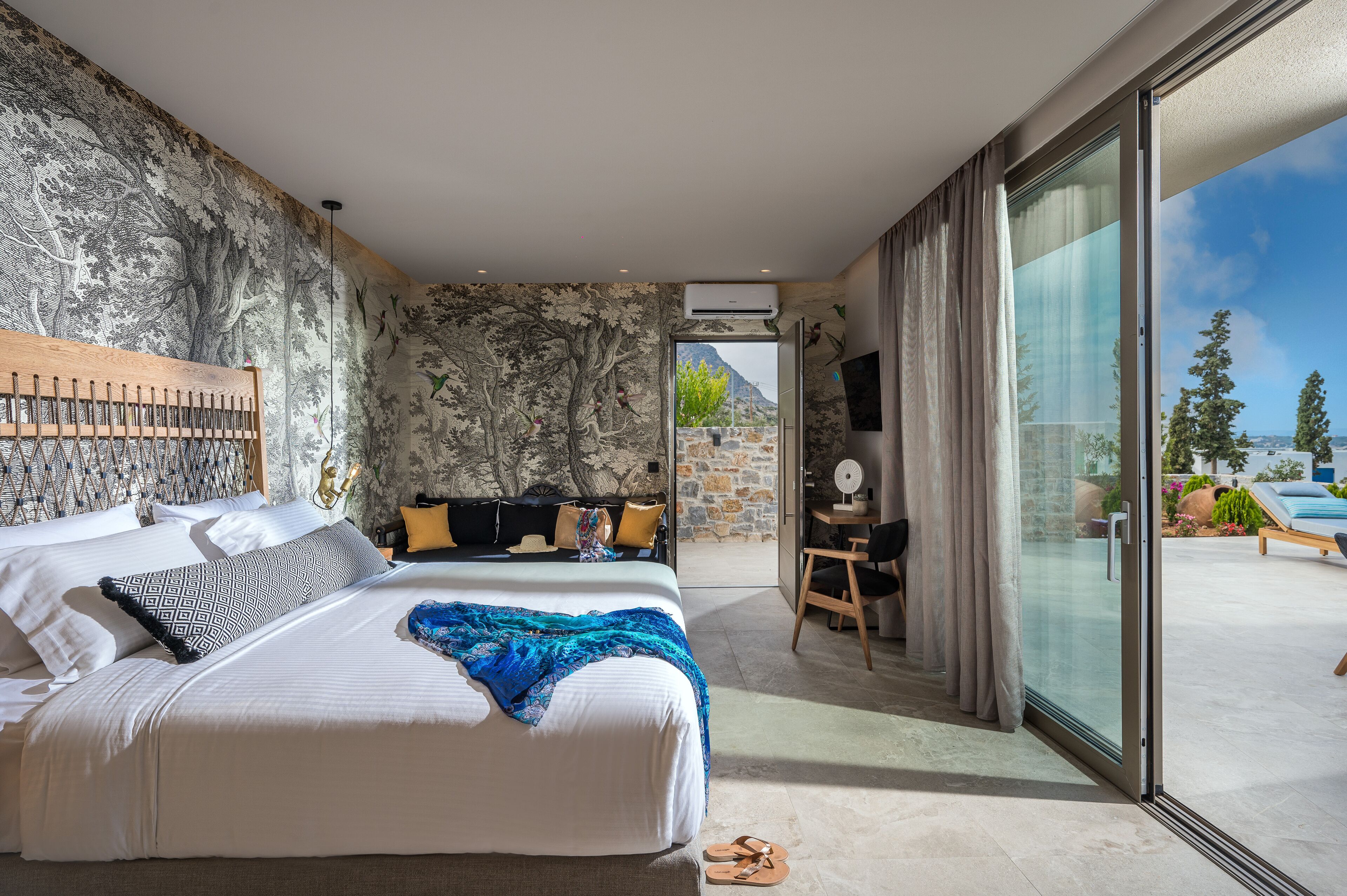 A modern bedroom with a large bed, a desk, and a view of the outdoors.