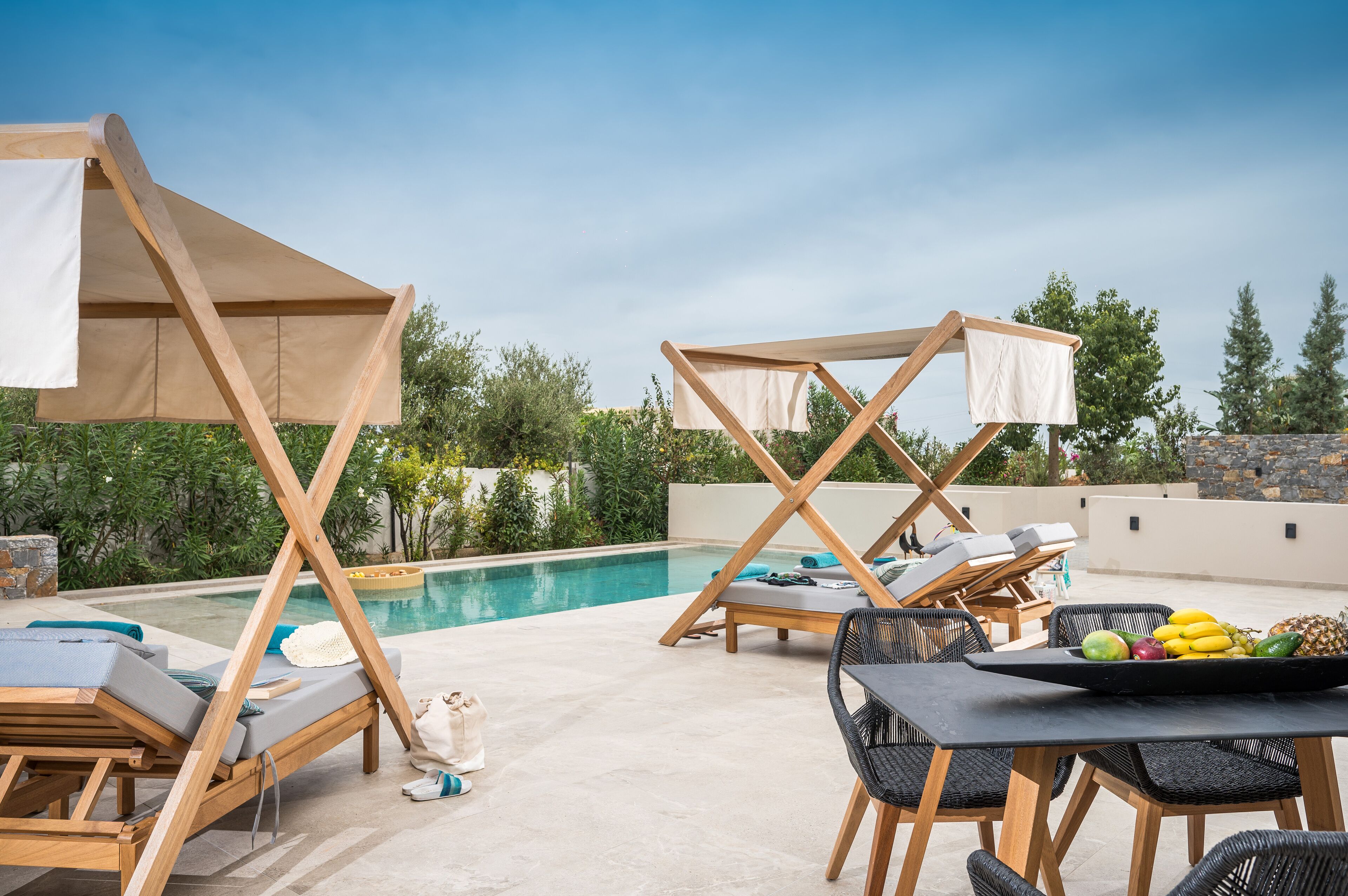 A poolside area with lounge chairs, a table with fruit, and a view of the pool and greenery.
