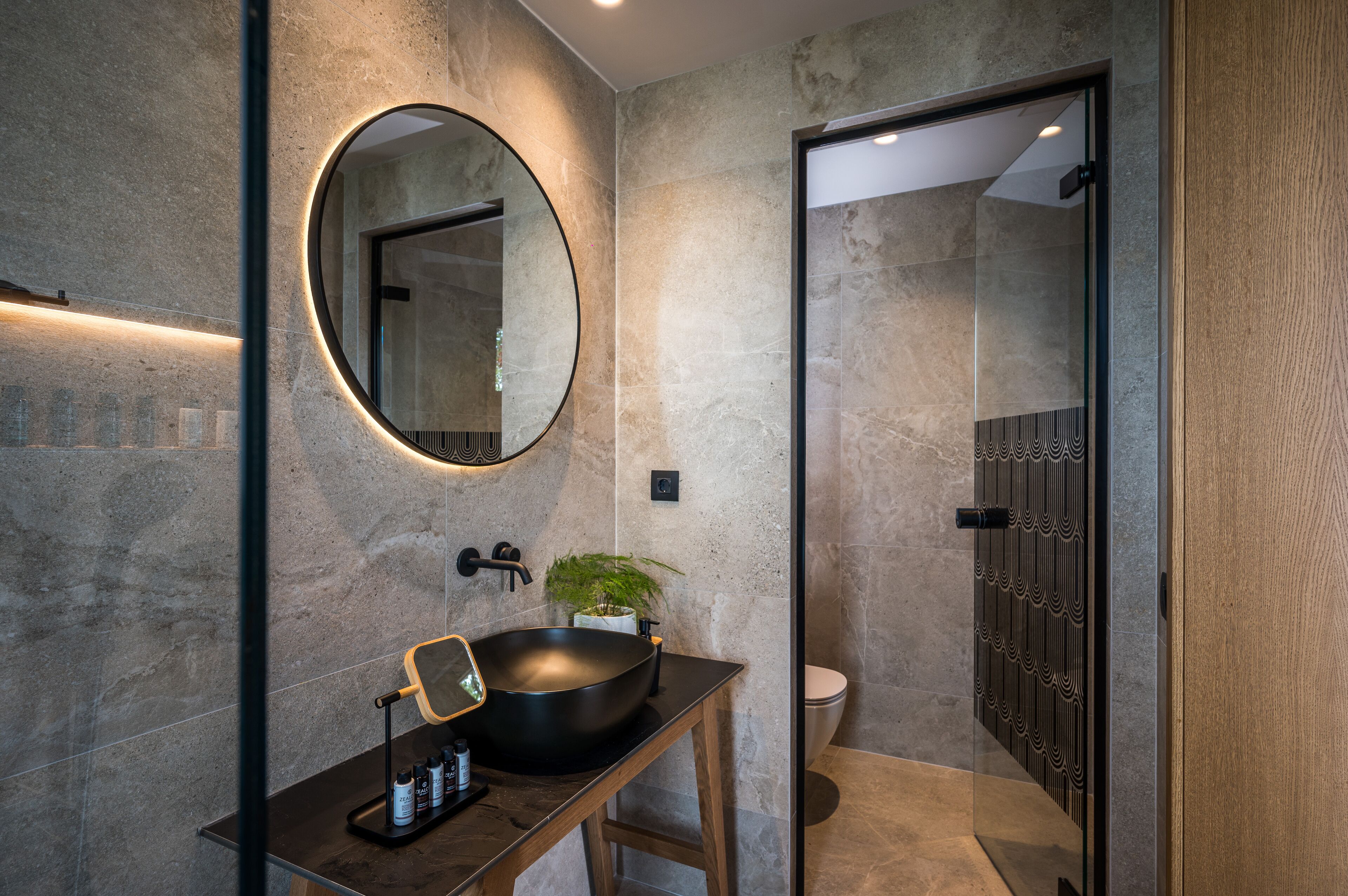 Un baño moderno con un espejo redondo, un lavabo negro y una planta en maceta.