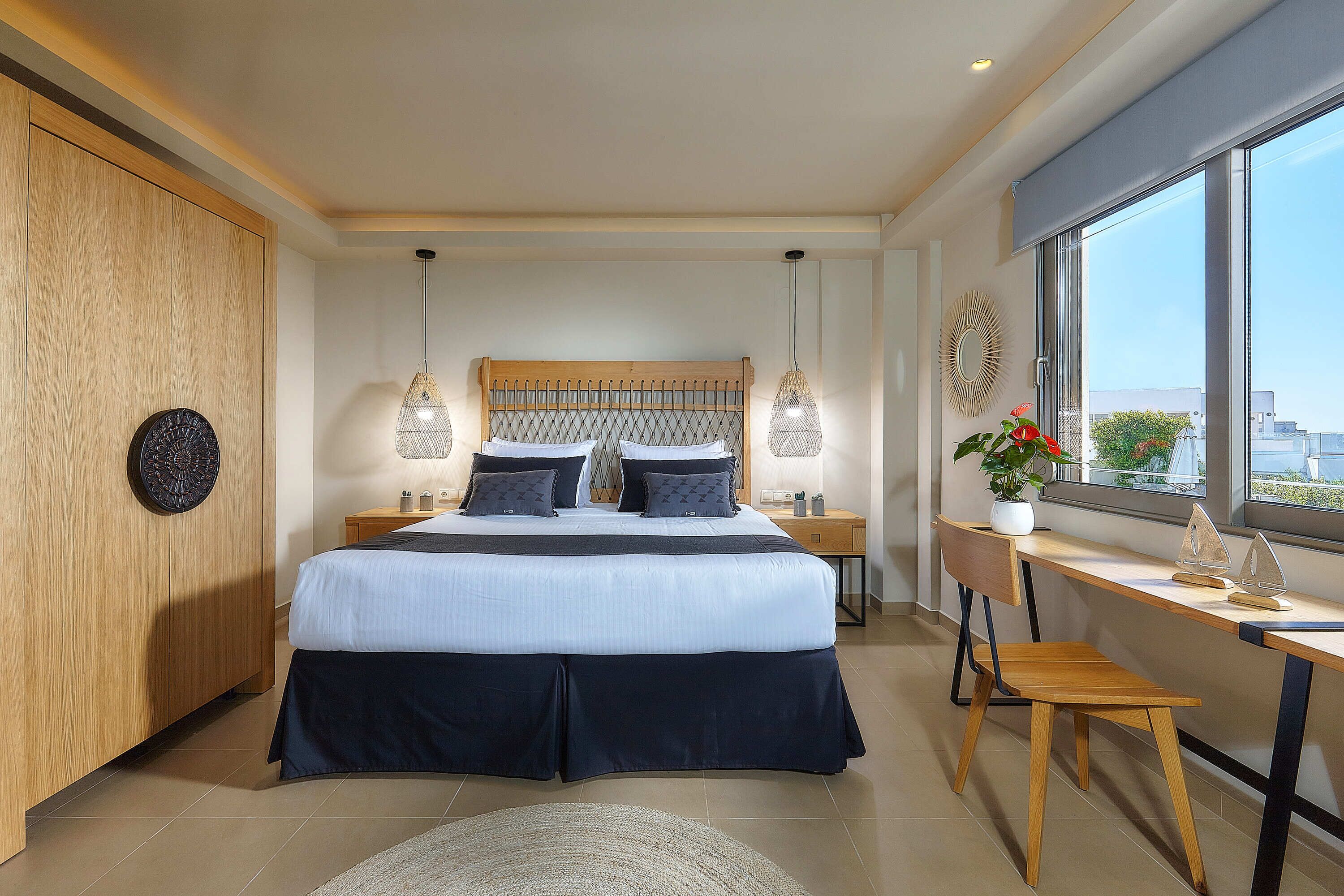 A modern bedroom with a large bed, bedside tables, a desk, and a view of the city through large windows.