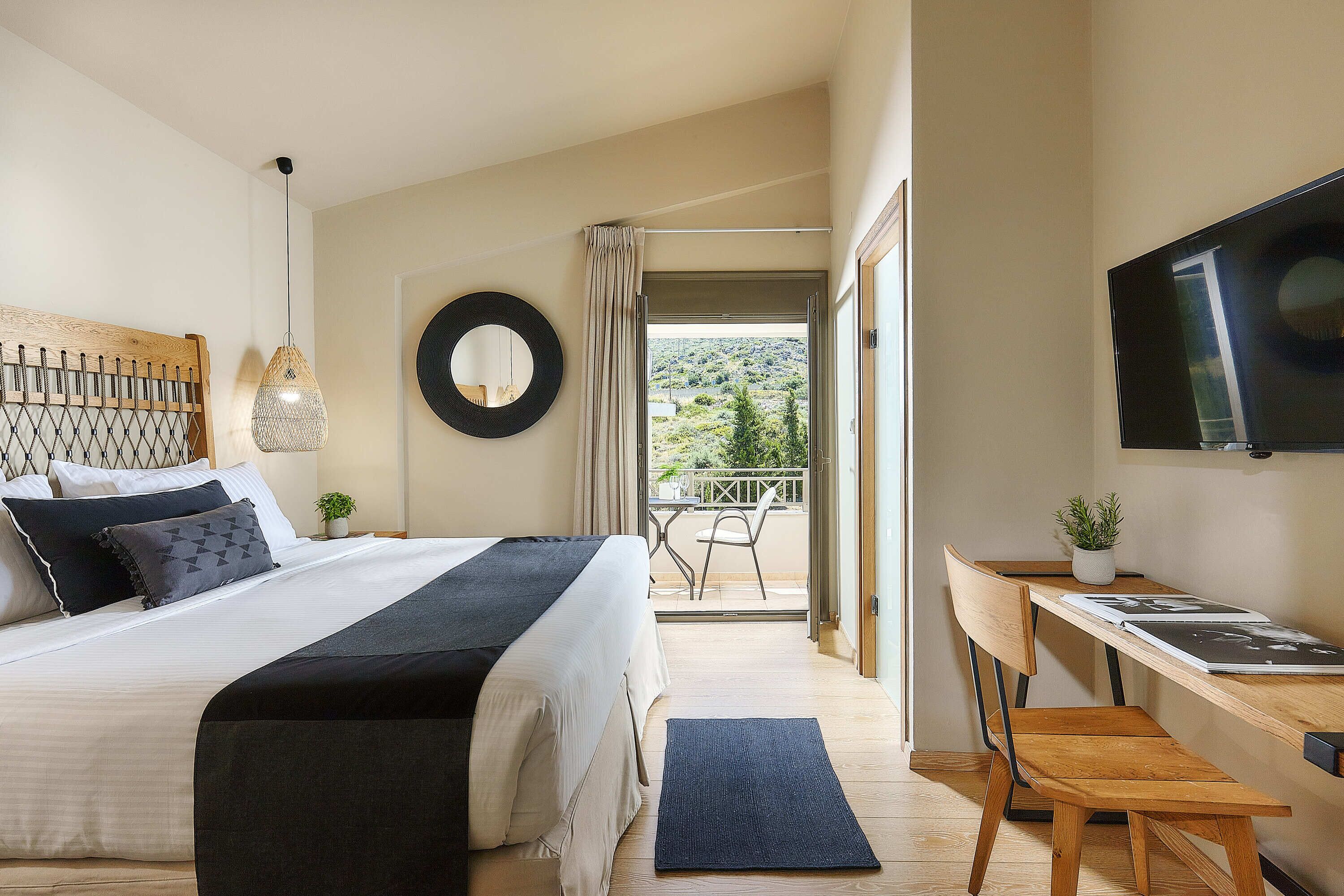 Une chambre avec un lit, un bureau, une chaise, une télévision, un balcon et une vue sur l’extérieur.