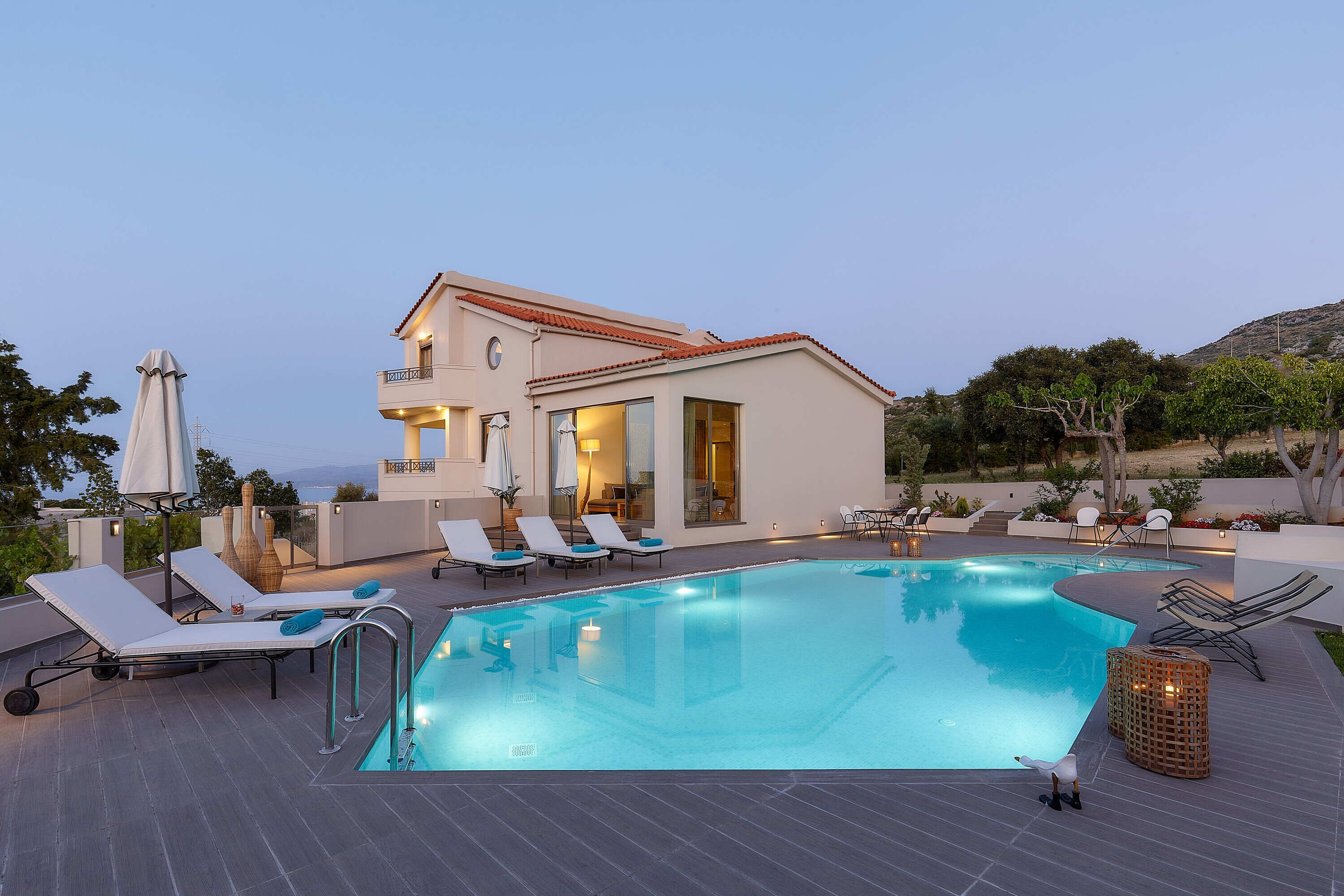 A modern house with a swimming pool, lounge chairs, and a view of the sea.