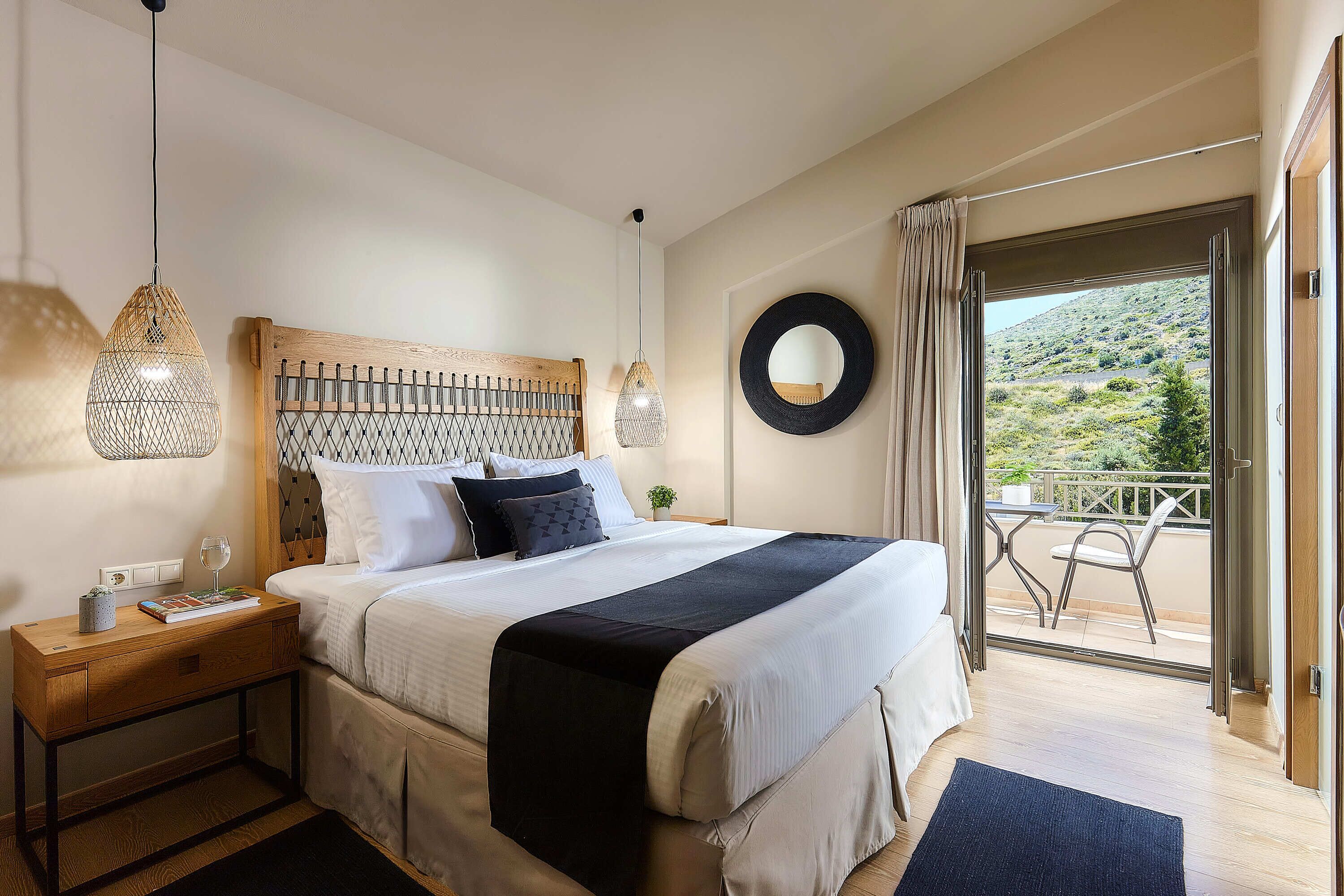 Un dormitorio con una cama grande, mesitas de noche, un tocador, un espejo redondo y vistas al exterior.