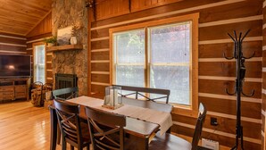 A wooden cabin interior with a dining table, chairs, a fireplace, and a stone wall. - 1 Relaxing Place - Quaint cottage, great mountain view, hot tub, and fire pit! Private! (Todd)