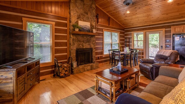 A cozy log cabin interior with a stone fireplace, wooden furniture, and large windows. - 1 Relaxing Place - Quaint cottage, great mountain view, hot tub, and fire pit! Private! (Todd)