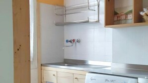 Uma cozinha compacta com máquina de lavar, armários de madeira, um esguicho metálico e painel de azulejos.