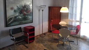 Uma sala de jantar com uma mesa redonda, cadeiras, um abajur e um quadro na parede.