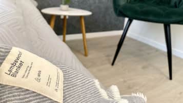 Une chambre avec un lit gris, une chaise verte, une petite table blanche ornée d’une plante et un mur gris à texture.