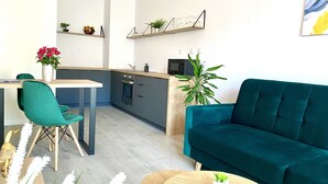 Eine moderne Küche mit Essbereich, einem blaugrünen Sofa und einem kleinen Tisch mit einer Pflanze.