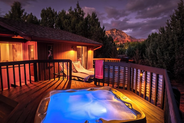 Een houten terras met een jacuzzi, lounge fauteuils en een houten chalet met balkon.