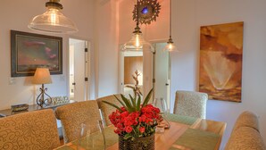 A dining area with a glass table, patterned chairs, a vase of red flowers, and pendant lights. - Luxury Sedona Home with Finnish Sauna and Hot Tub (Sedona)