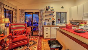 A cozy kitchen with a red chair, a dining area with a table and chairs, and a view of a garden through the sliding glass door. - Luxury Sedona Home with Finnish Sauna and Hot Tub (Sedona)