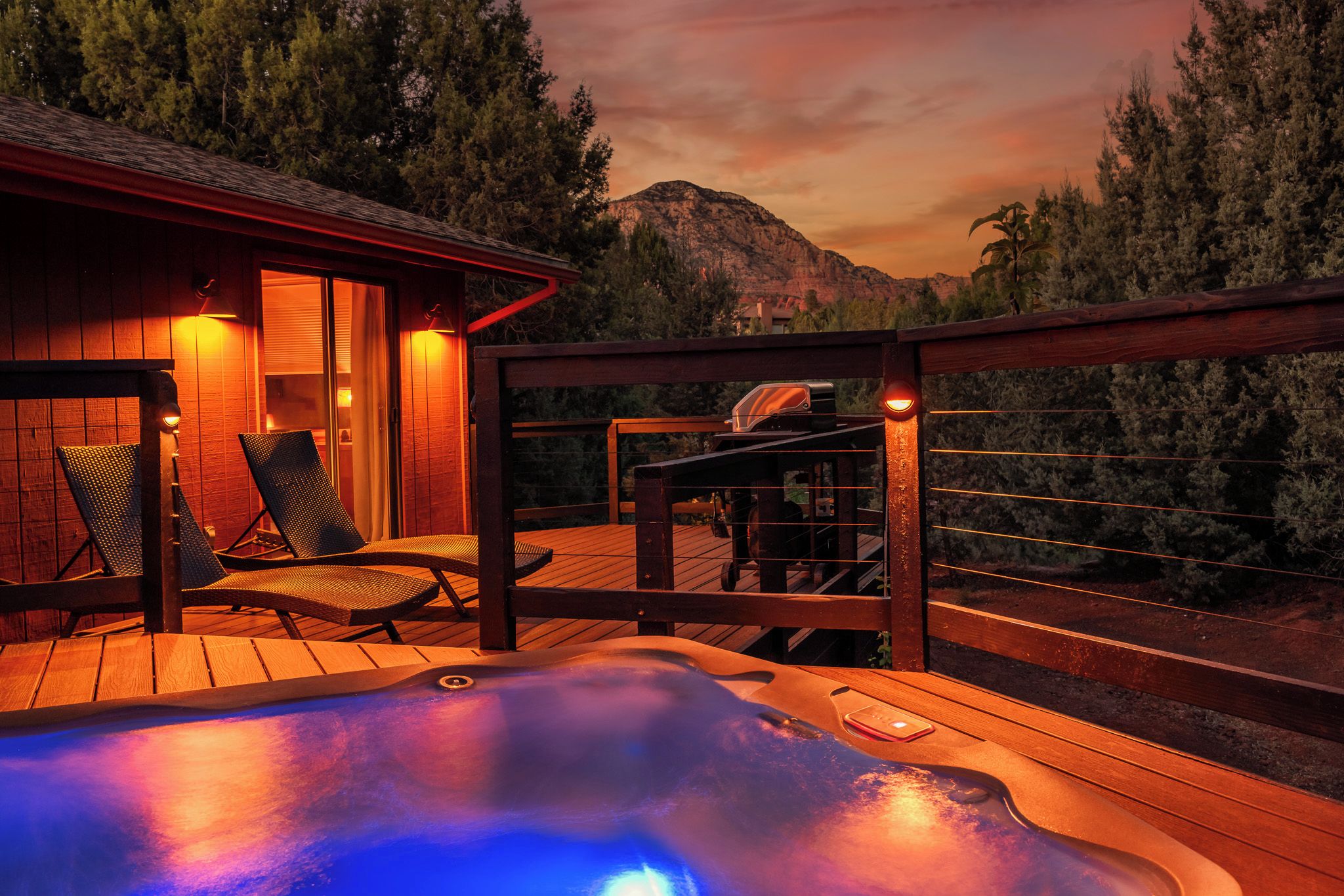 A hot tub on a wooden deck with lounge chairs, a barbecue grill, and a mountain view.