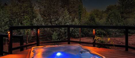 A hot tub on a wooden deck with a night sky view.