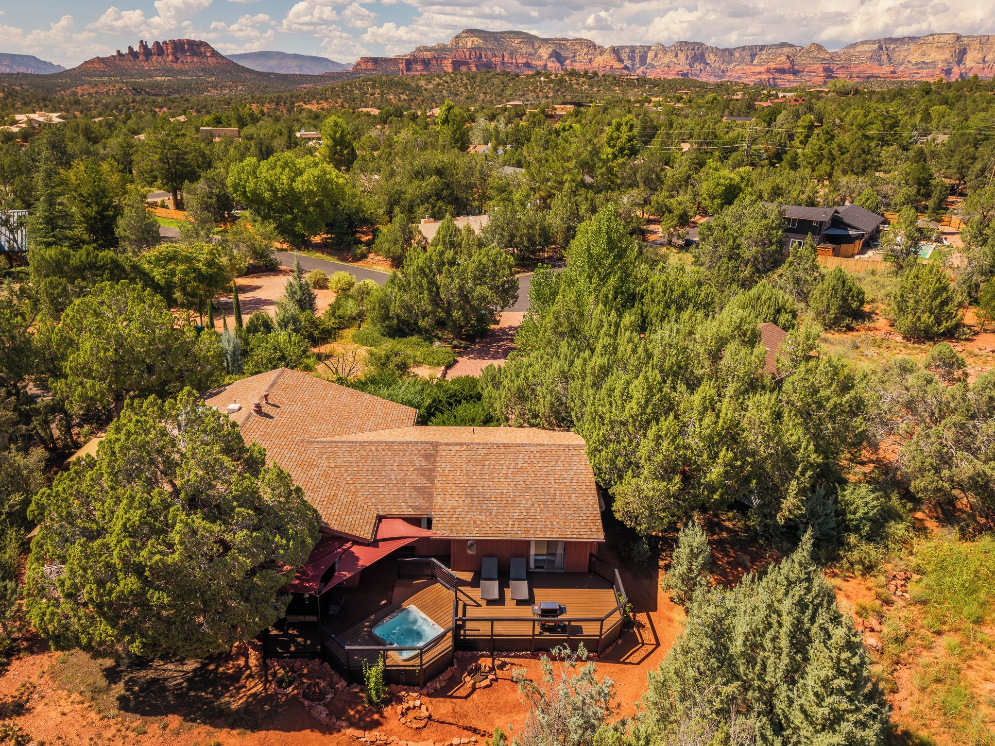 A house with a large deck and a hot tub, surrounded by trees and a desert landscape.