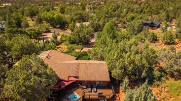 A house with a large deck and a hot tub, surrounded by trees and a desert landscape.