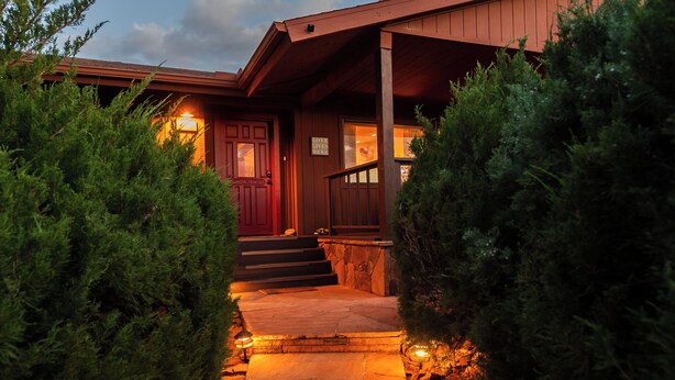 A wooden house with a red door, a stone pathway, and a 'Love Lives Here' sign. - Luxury Sedona Home with Finnish Sauna and Hot Tub (Sedona)
