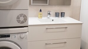 Un área de lavandería con lavadoras apiladas, un lavamanos y un espejo encima.