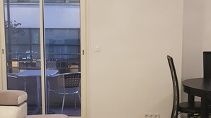 Una sala de estar con un sofá, una mesa de comedor con sillas, una alfombra roja y un ventanal corredizo que da a un espacio exterior.