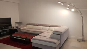 Una sala de estar moderna con un sofá seccional, una mesa de centro de vidrio, una alfombra roja, un televisor sobre un soporte negro y una lámpara de pie.