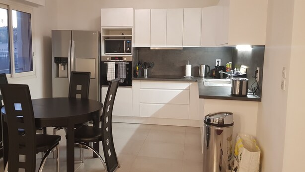 Una cocina moderna con gabinetes blancos, un microondas empotrado y un refrigerador de acero inoxidable.