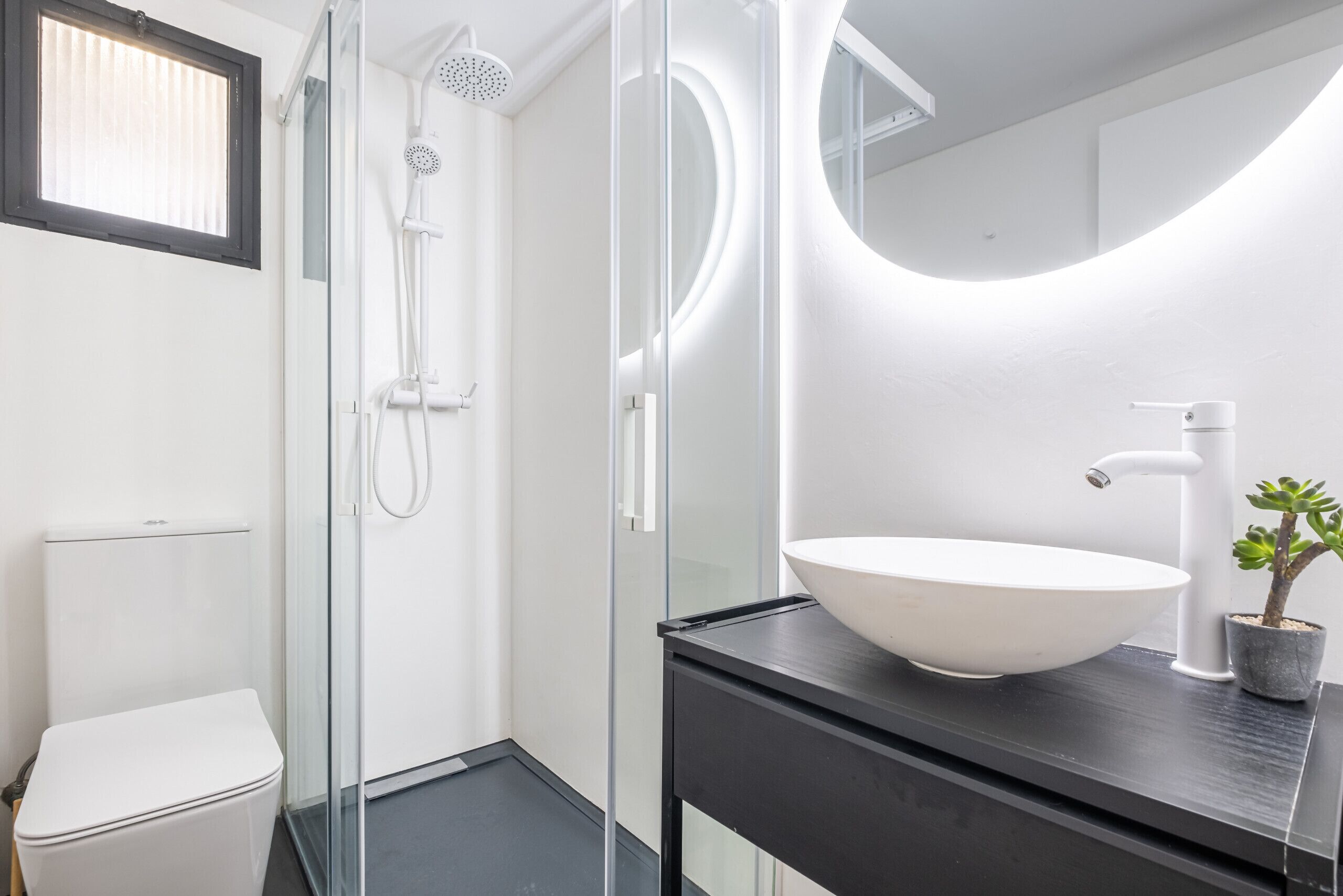 A modern bathroom with a glass-enclosed shower, a white toilet, and a large white sink on a black countertop.
