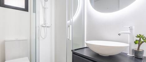 A modern bathroom with a glass-enclosed shower, a white toilet, and a large white sink on a black countertop.