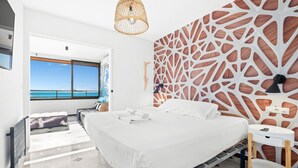 Una habitación de hotel moderna con una cama grande, una mesita de noche pequeña, vistas al océano y un diseño de pared original.