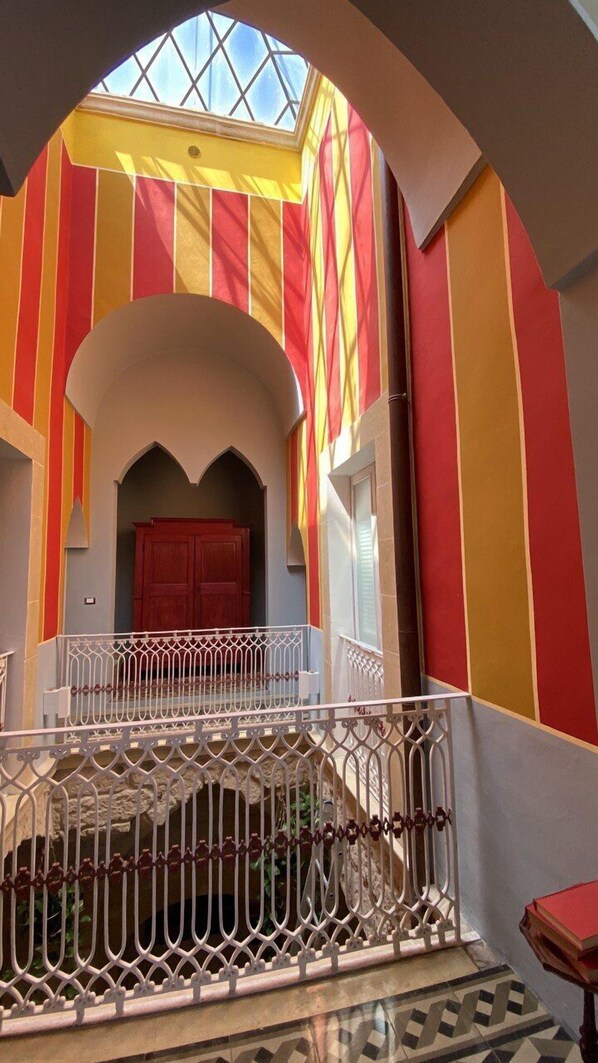 A staircase with a white railing leading to a red door, surrounded by walls with vertical stripes in red, yellow, and orange.