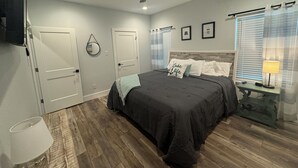 Quarto com cama, ventilador de teto, mesa de cabeceira com abajur e janela com persianas.