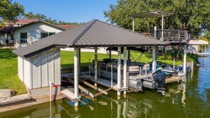 Um cais com barcos e uma área coberta à beira de um lago, cercado por casas.