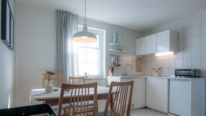 Une cuisine moderne avec des meubles blancs, une table à manger avec des chaises, une poubelle noire et une fenêtre avec des rideaux.