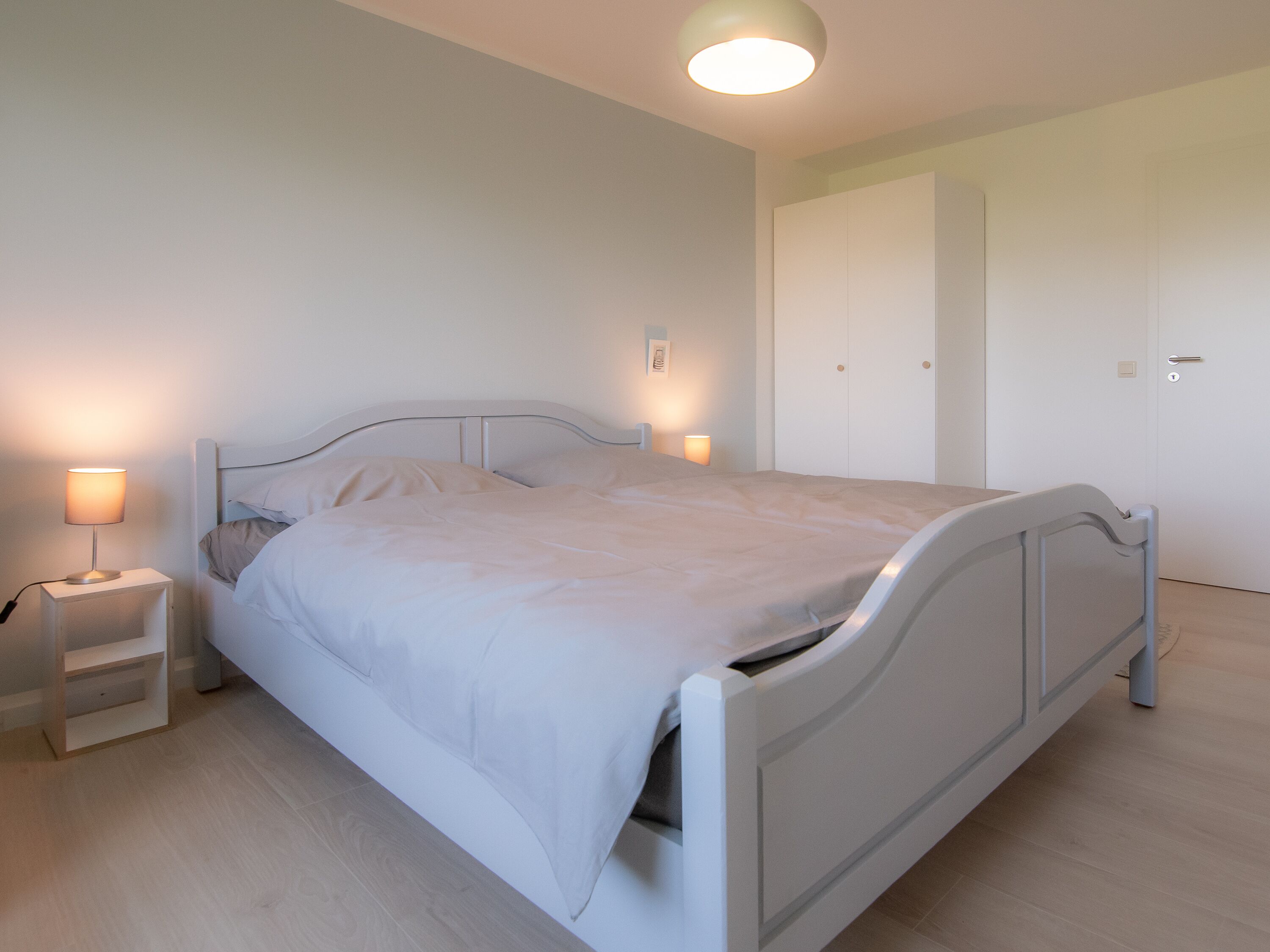 Une chambre à coucher moderne et minimaliste, avec un lit simple, des lampes de chevet et une armoire.