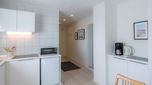 Une cuisine compacte avec des meubles blancs, un grille-pain encastré, une machine à café et un petit réfrigérateur.