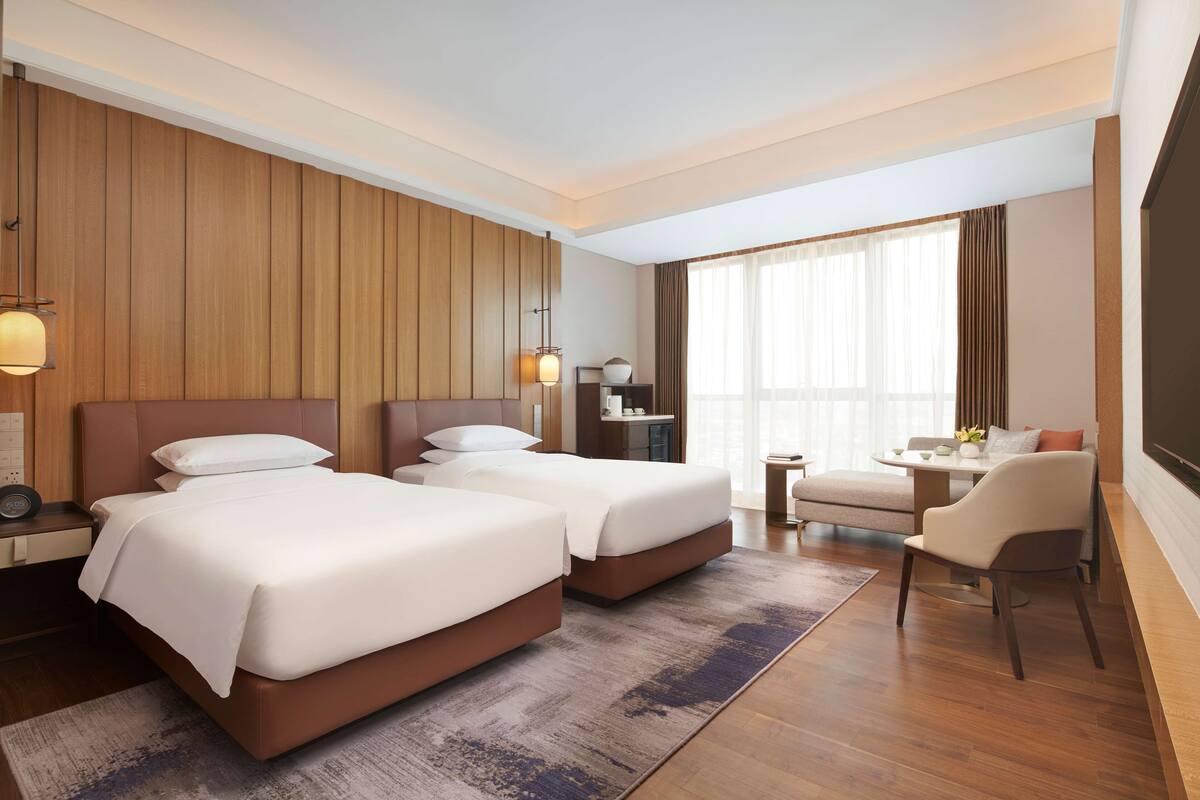 Une chambre d’hôtel avec deux lits, un bureau, une chaise et une grande fenêtre.