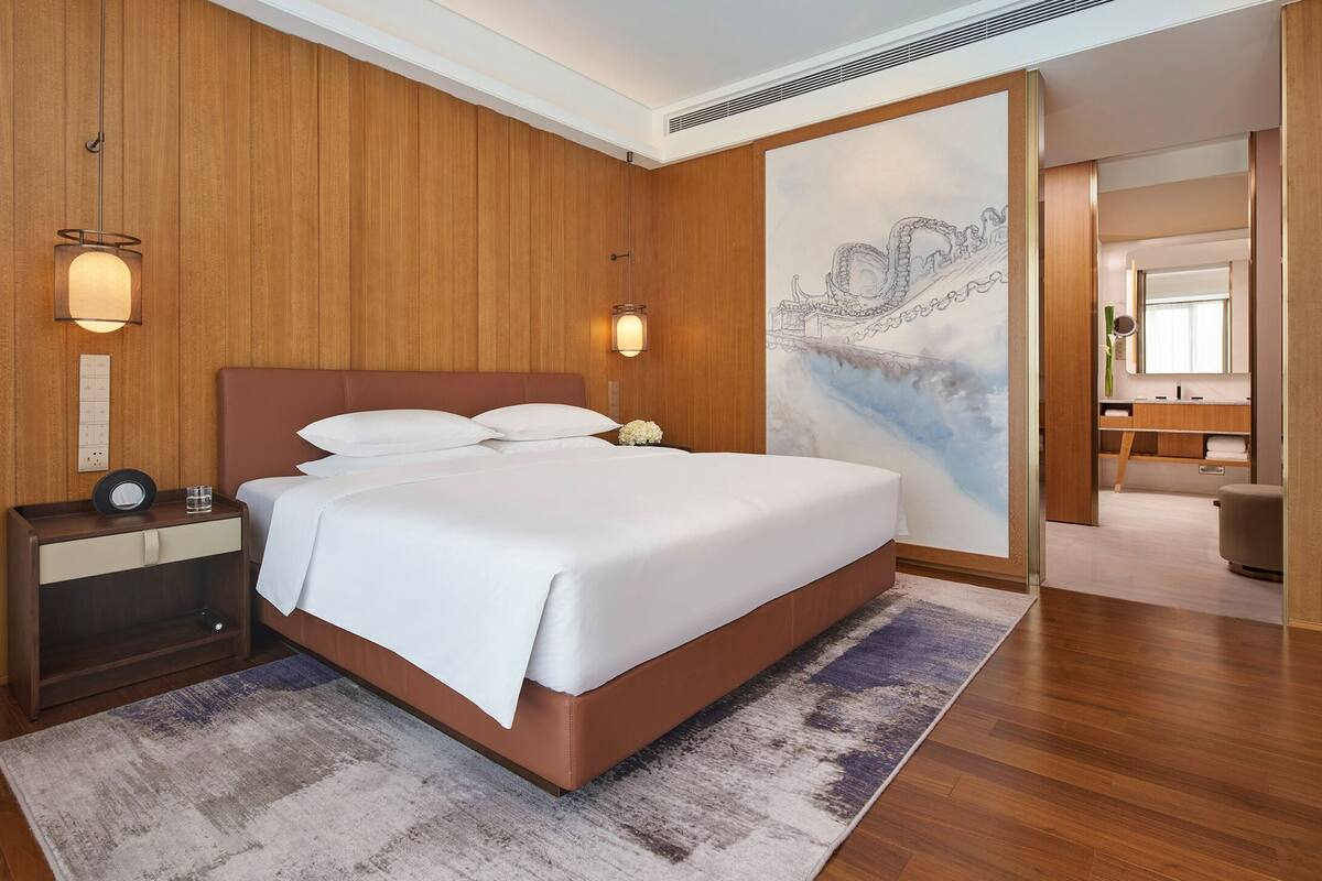 Une chambre d’hôtel avec un grand lit, des murs recouverts de lambris en bois, une table de chevet avec une lampe et un tableau accroché au mur.