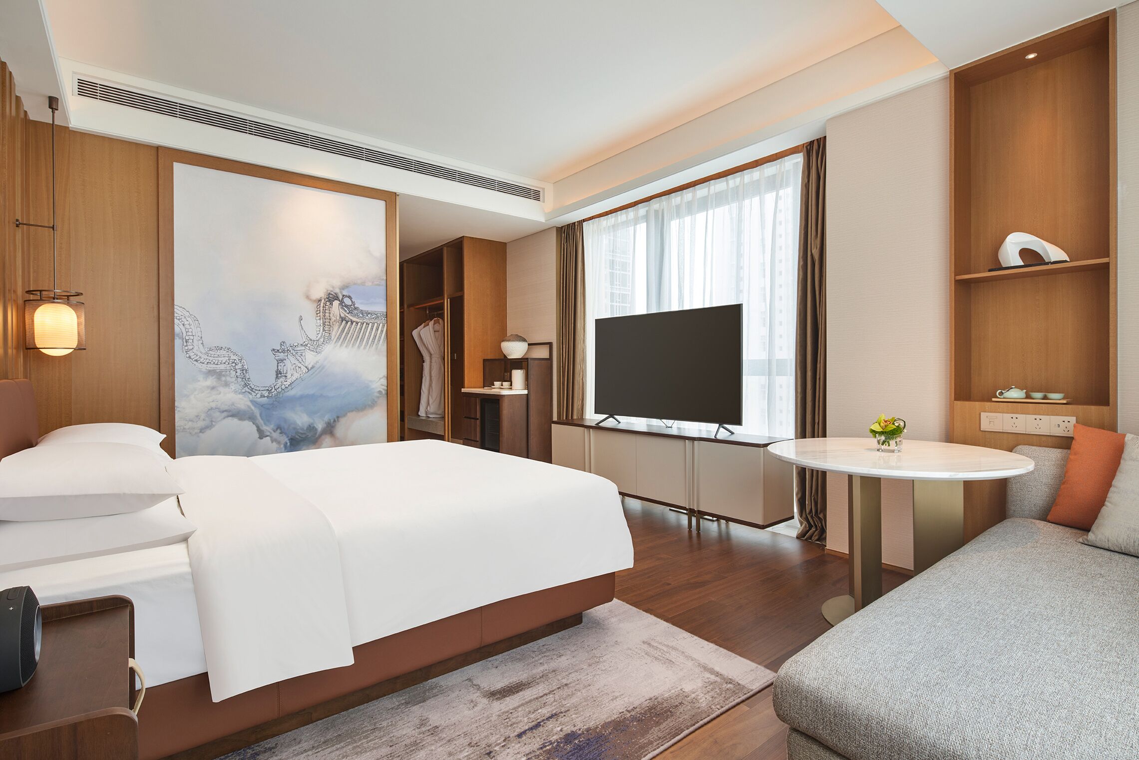 A modern hotel room with a large bed, a sofa, a TV, and a small table.