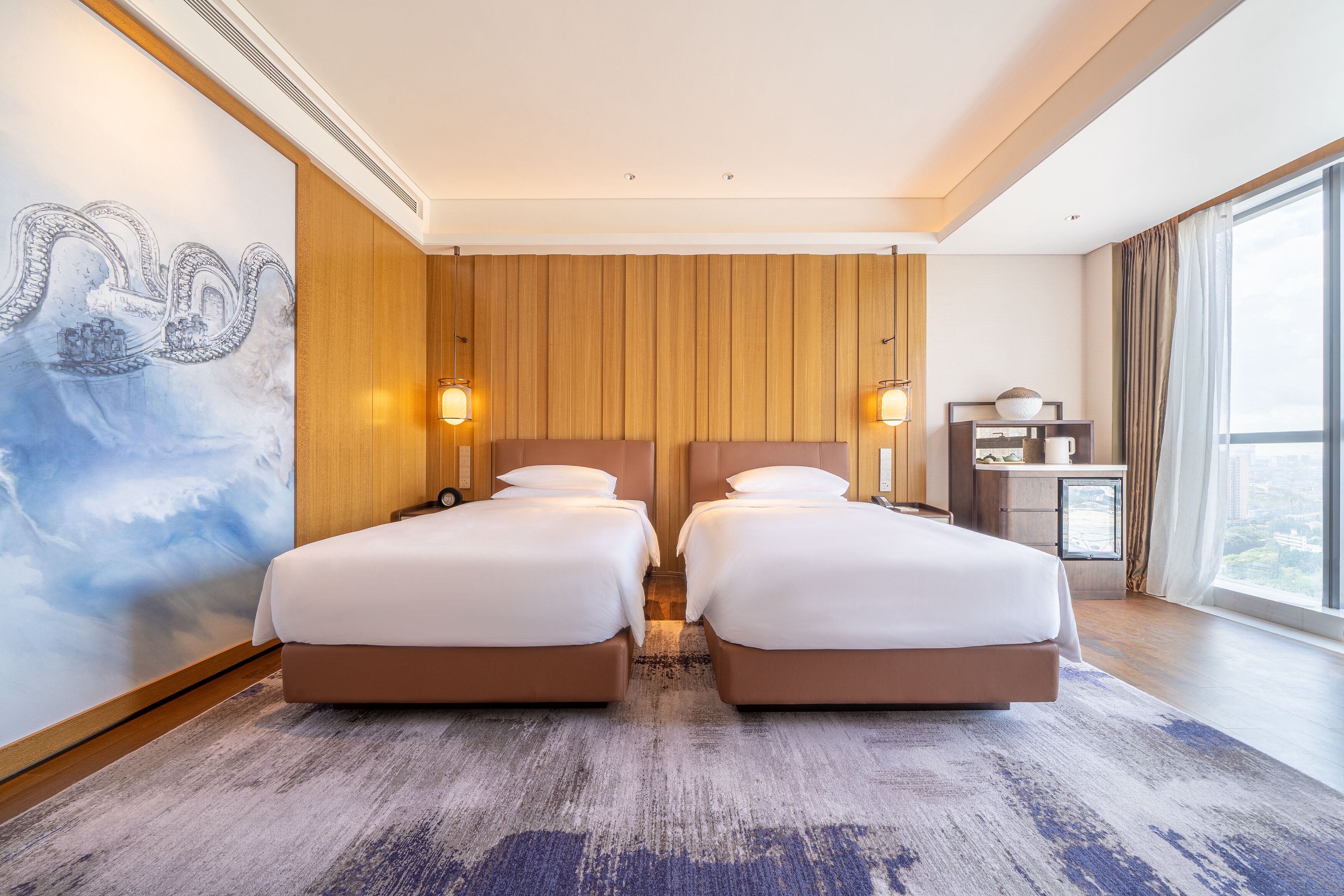 Una habitación de hotel con dos camas, paneles de madera, un ventanal grande y un mural en la pared.