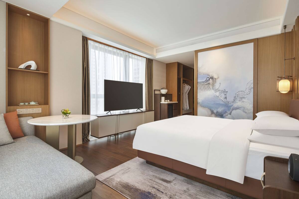 Une chambre d’hôtel moderne avec un grand lit, un canapé, une télévision et un tableau au mur.