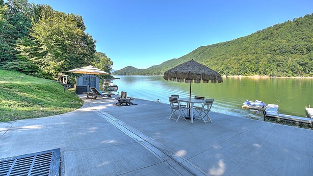 A lakeside patio with a thatched umbrella, seating, and a small building, likely a restroom.