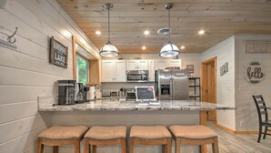 A kitchen with wooden walls, a marble countertop, and bar stools.