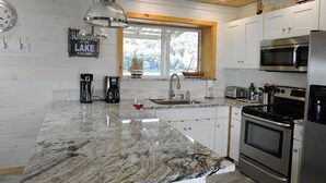 A kitchen with a large granite countertop, stainless steel appliances, and a window with a view of a lake.