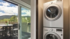 A laundry room with stacked front-loading washers and dryers, a sliding glass door leading to an outdoor patio with a table and chairs, and a view of mountains in the background. - Vail 21 407 - 2 Bedroom Diamond (Vail)